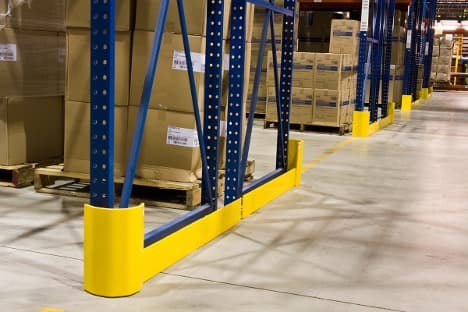 Rack protection guard bolted at the base of a pallet rack upright — absorbing forklift impacts to prevent structural damage